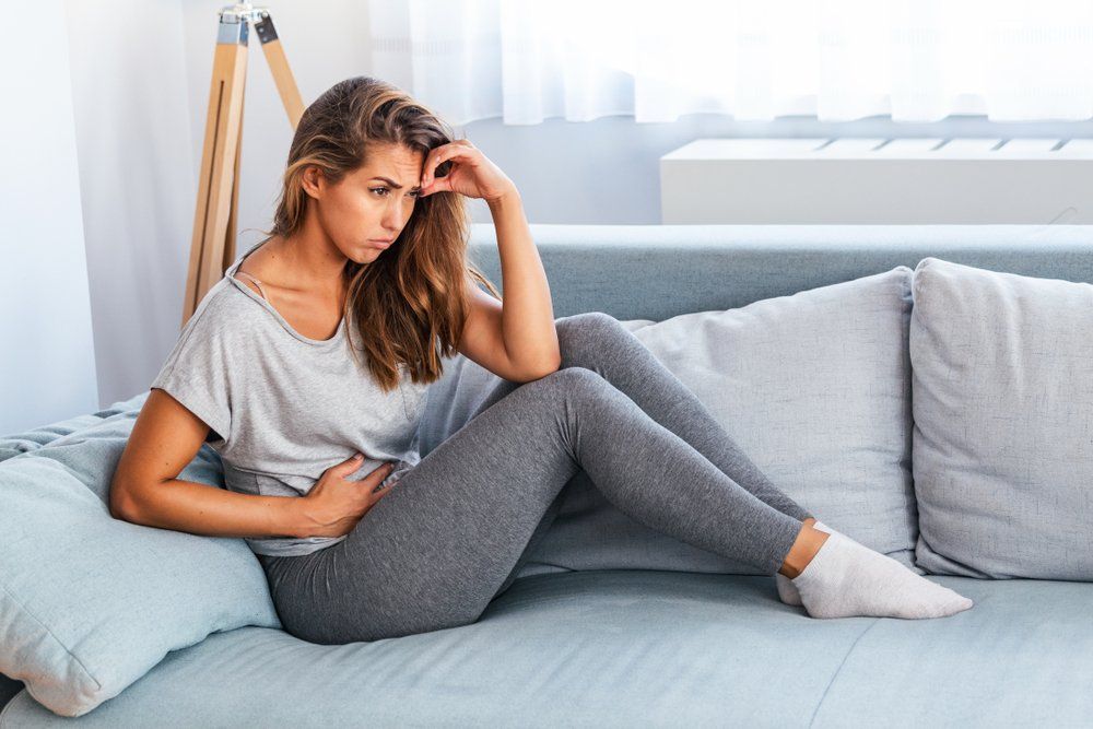 A woman is sitting on a couch with her hands on her stomach — Colonic Healthcare in Rosslea, QLD