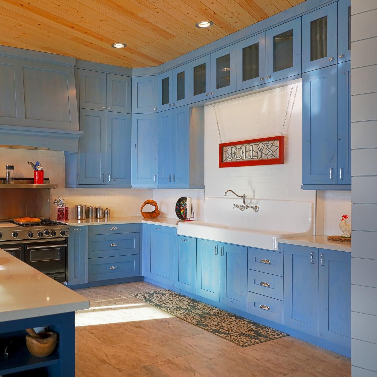 Bright blue kitchen with white farmhouse sink, wood ceiling, and red wall art