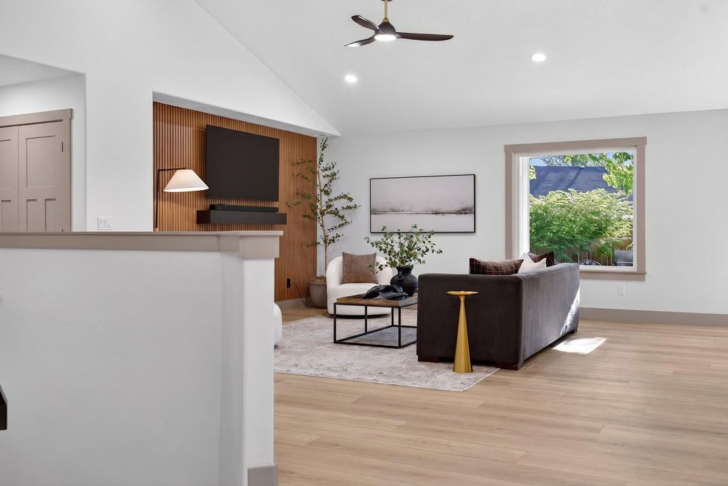 Bright open living room with gray sofa, wood floors, and large window overlooking greenery