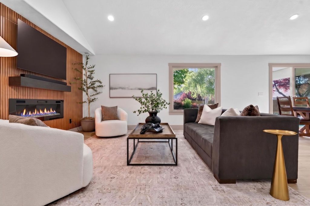 Modern living room with fireplace, gray sofa, white chair, coffee table, and large window views