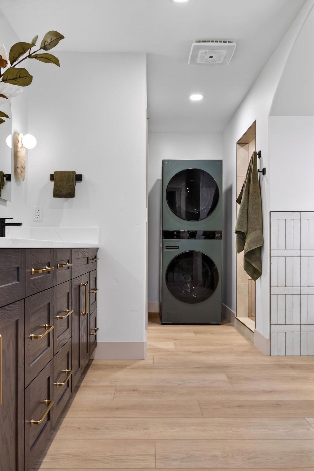 Modern laundry room with stacked washer and dryer in a narrow hallway, wood floors, and dark cabinets