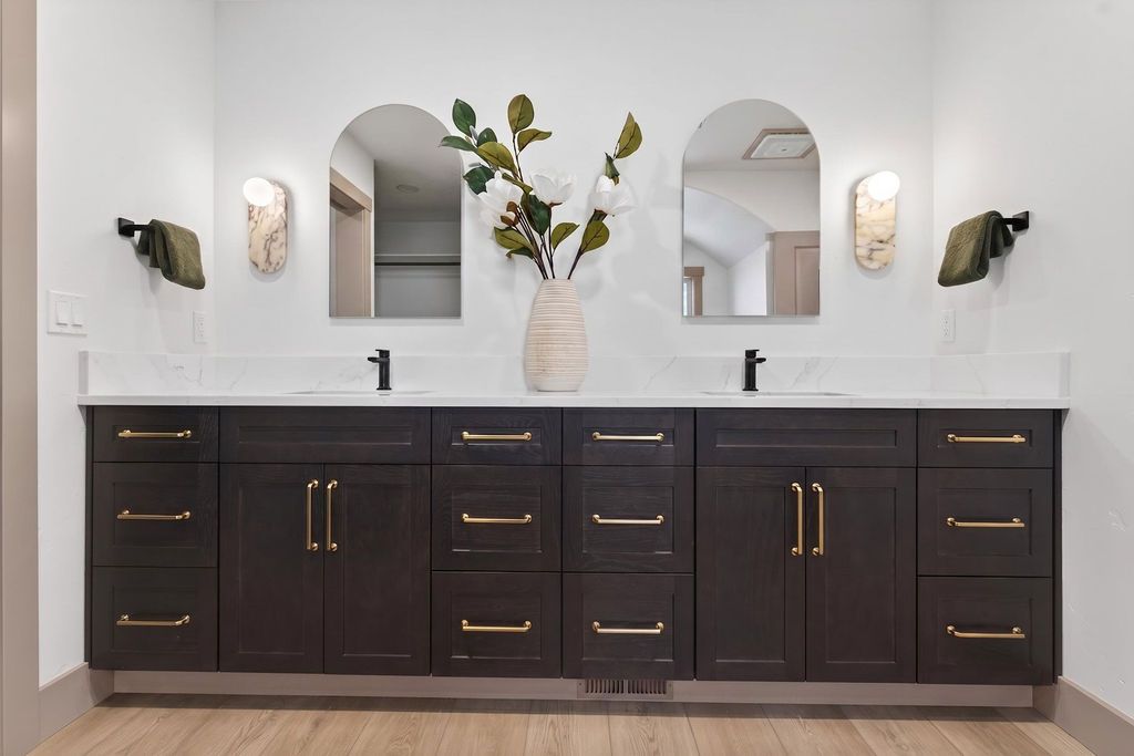 Modern bathroom vanity with dark cabinets, white countertop, dual mirrors, and a vase of greenery