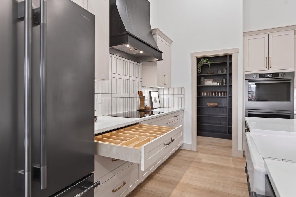 Bright modern kitchen with black fridge, white cabinets, oven, and island with tray of pastries