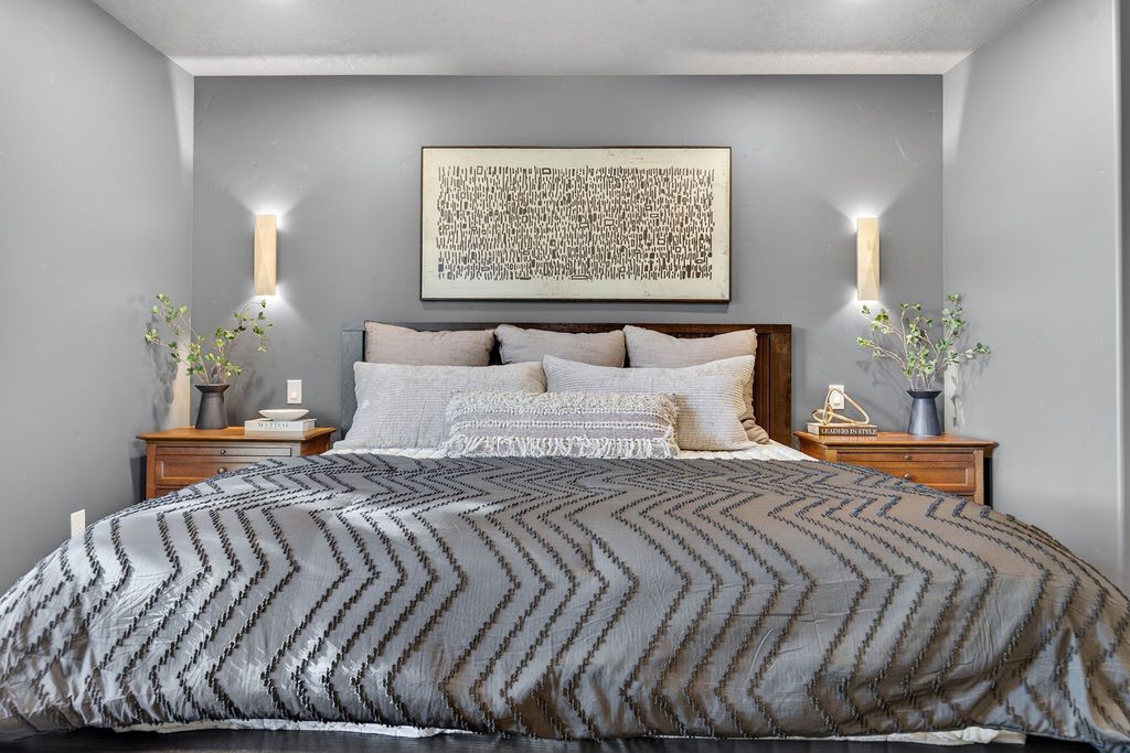 Modern gray bedroom with a king bed, patterned bedding, wooden nightstands, and wall sconces