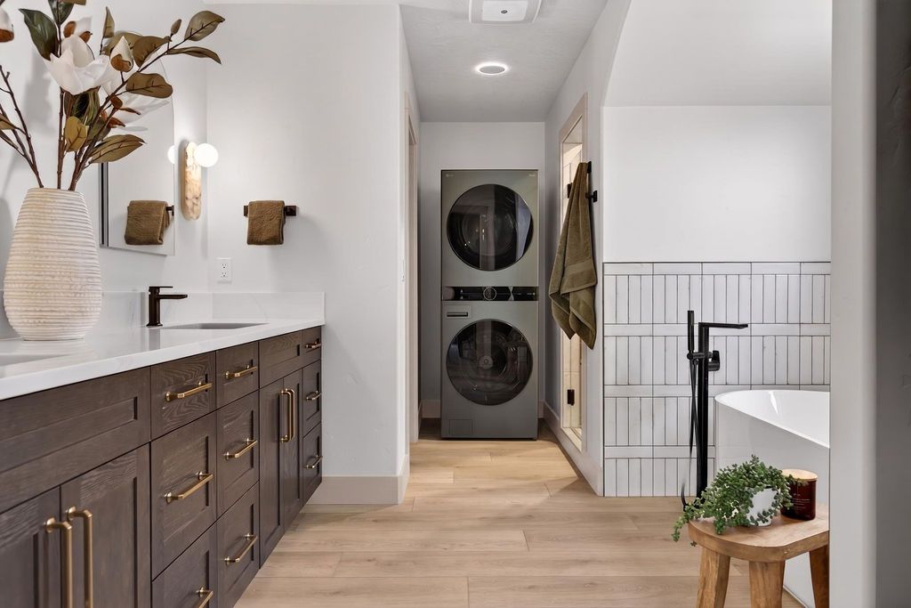 Modern laundry room with dark wood cabinets, white walls, stacked washer-dryer, and staircase railing