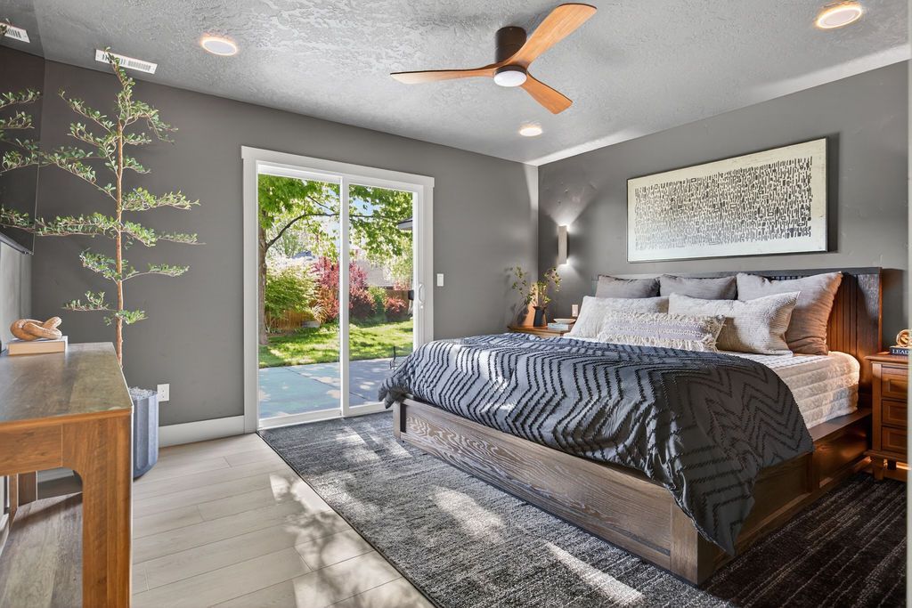 Modern gray bedroom with king bed, ceiling fan, French doors, and a plant on a wooden dresser