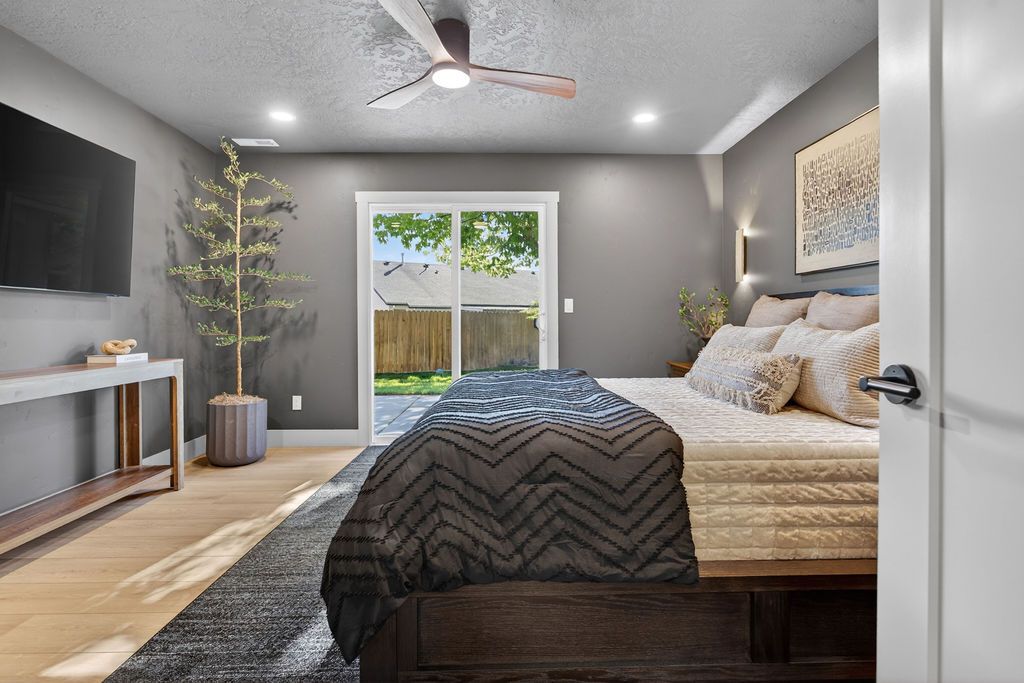 Modern bedroom with gray walls, a bed, TV console, ceiling fan, and sliding glass doors to a patio