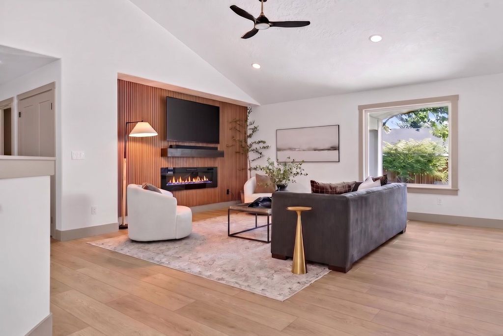 Bright modern living room with gray sofa, white chair, wood fireplace, and large window