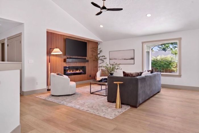 Bright modern living room with gray sofa, white chair, wood fireplace, and large window views