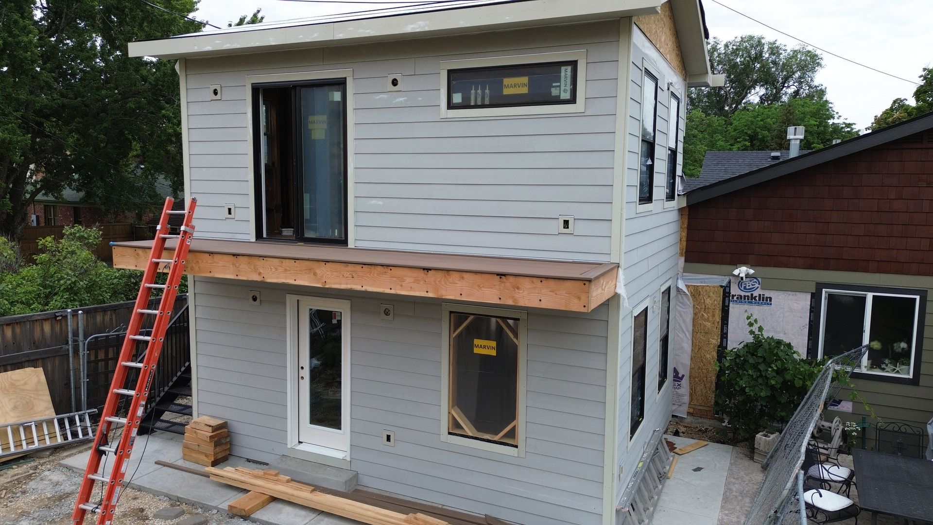 Partially renovated two-story house with white siding, exposed trim, and ladders on the front