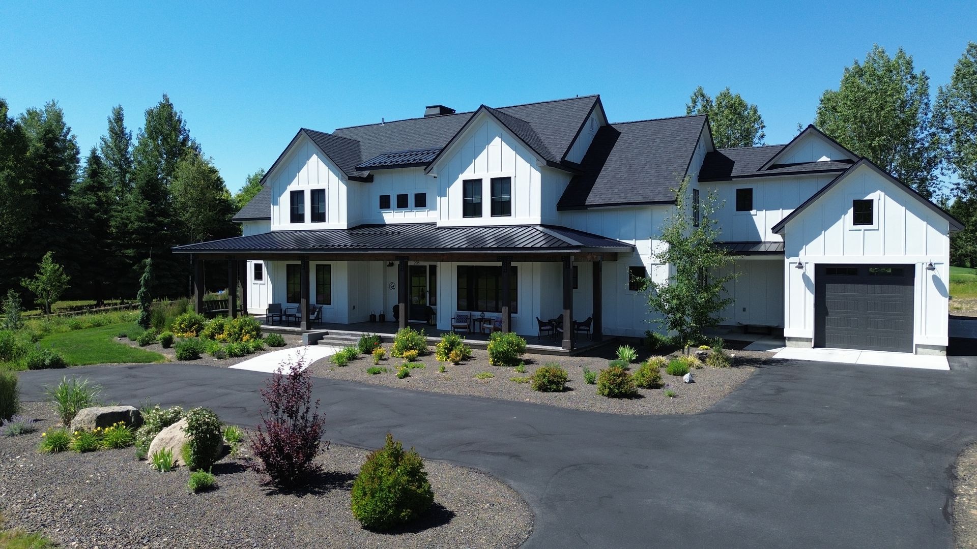 Large white two-story house with a porch, attached garage, and landscaped driveway under a blue sky