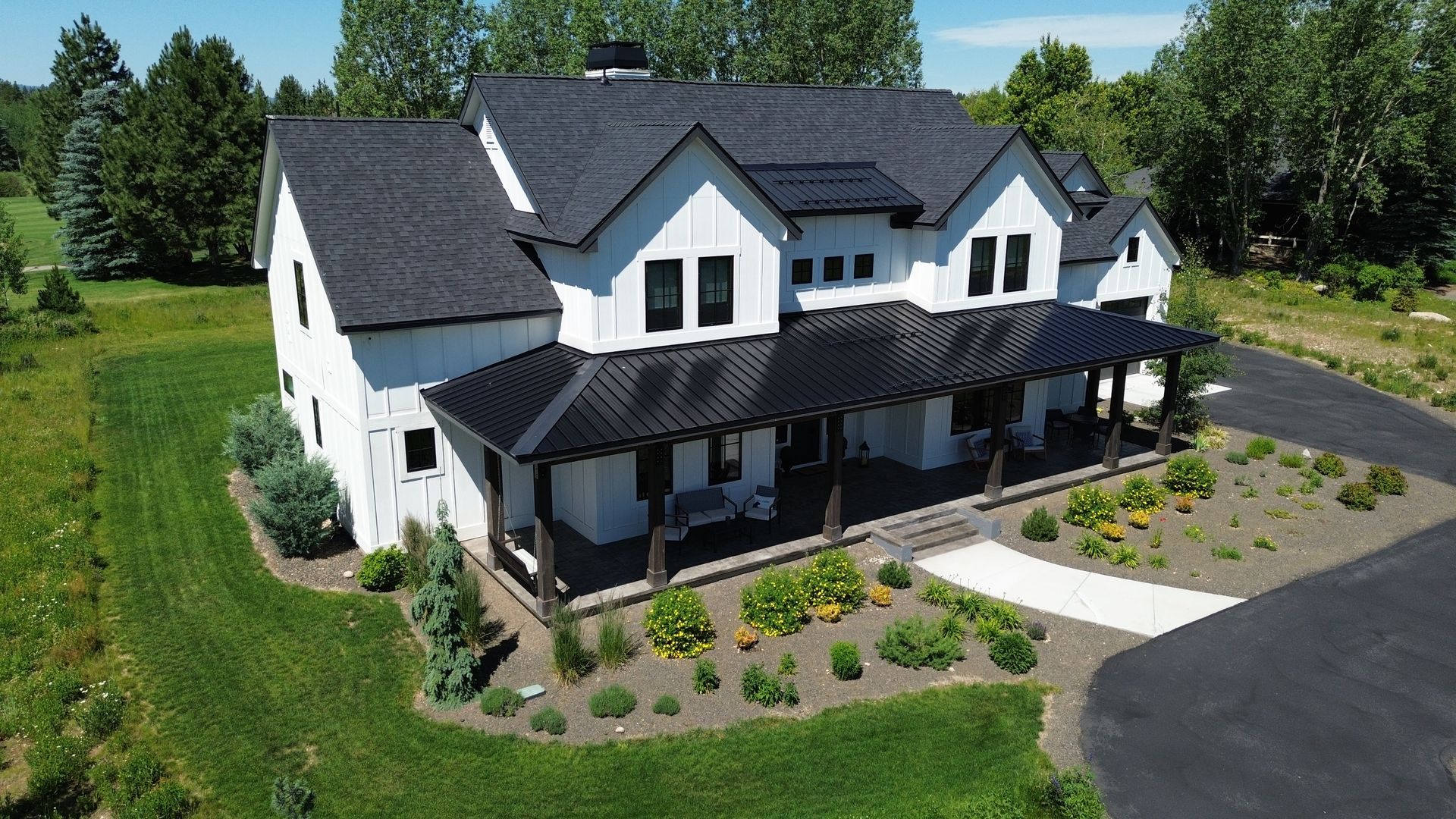 Large white two-story house with dark roof and front porch, surrounded by trees and a landscaped lawn