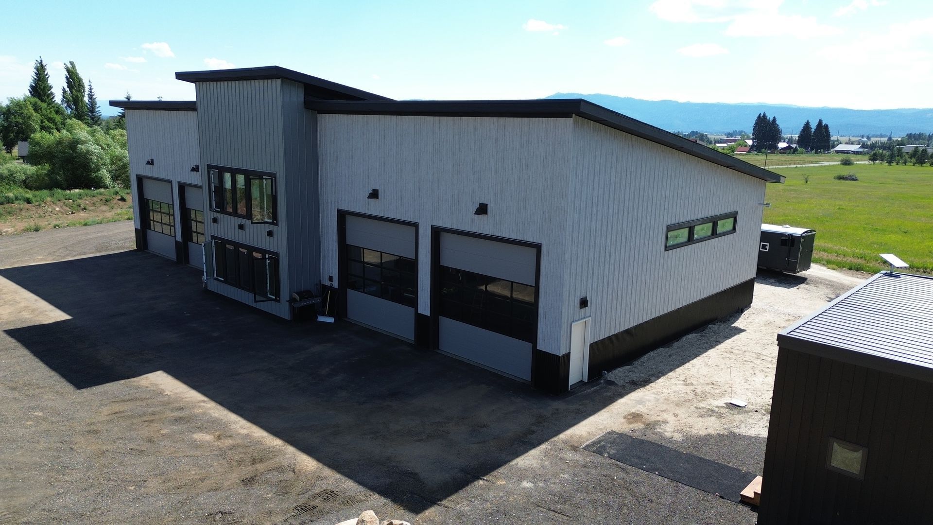 White industrial building with garage doors and windows on a gravel lot under a clear sky