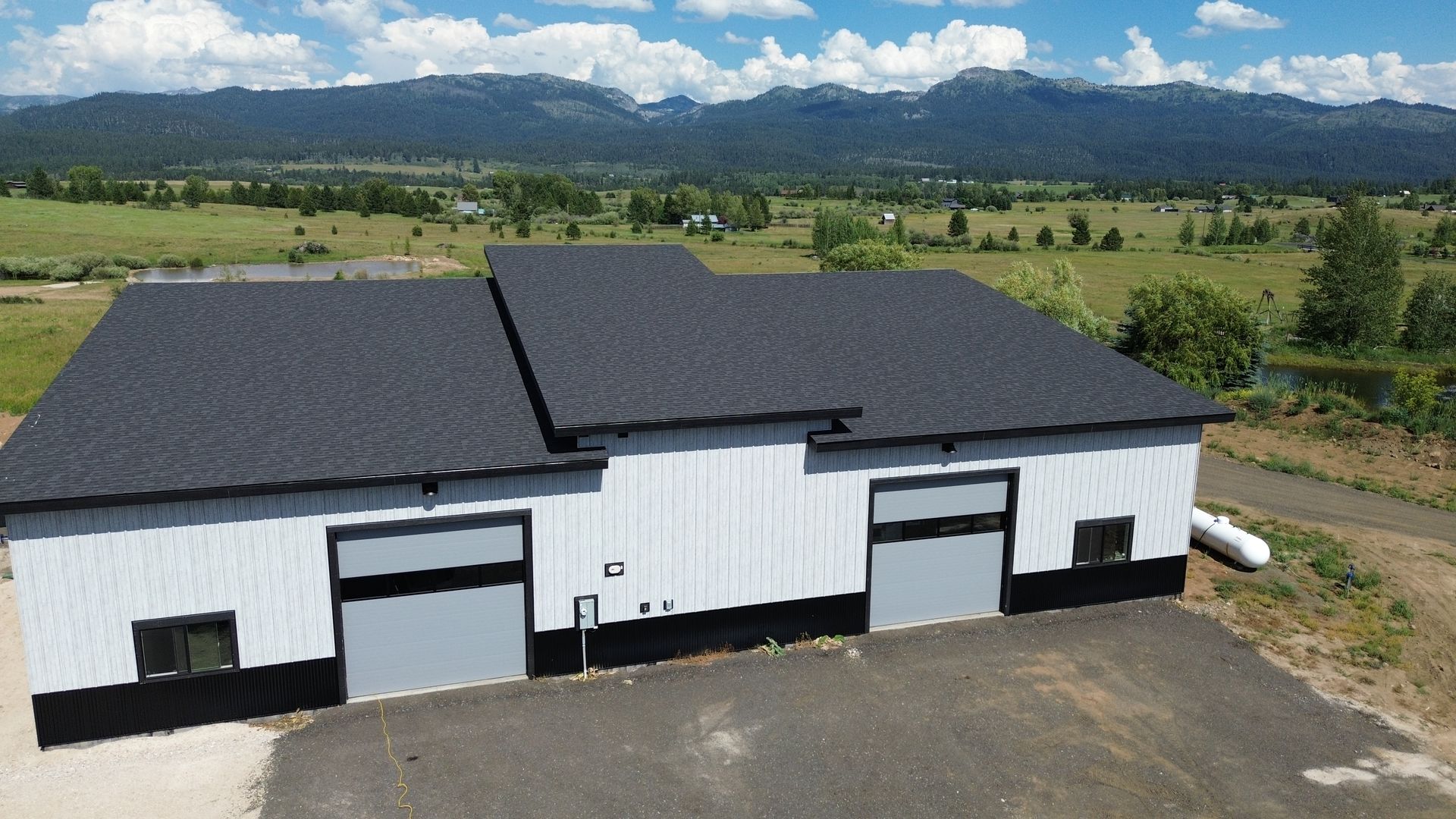 White industrial building with black roof in a rural landscape, mountains in the background