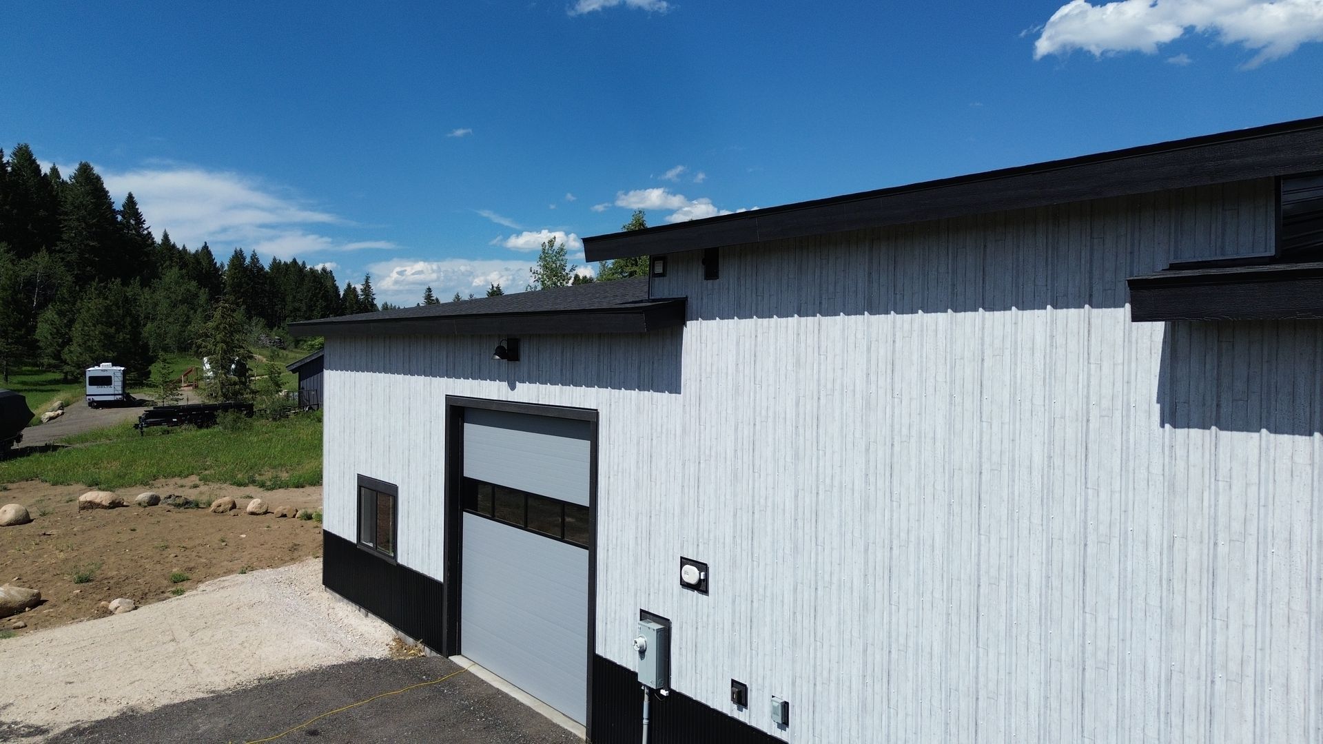 White industrial building with black trim beside a gravel lot under a blue sky