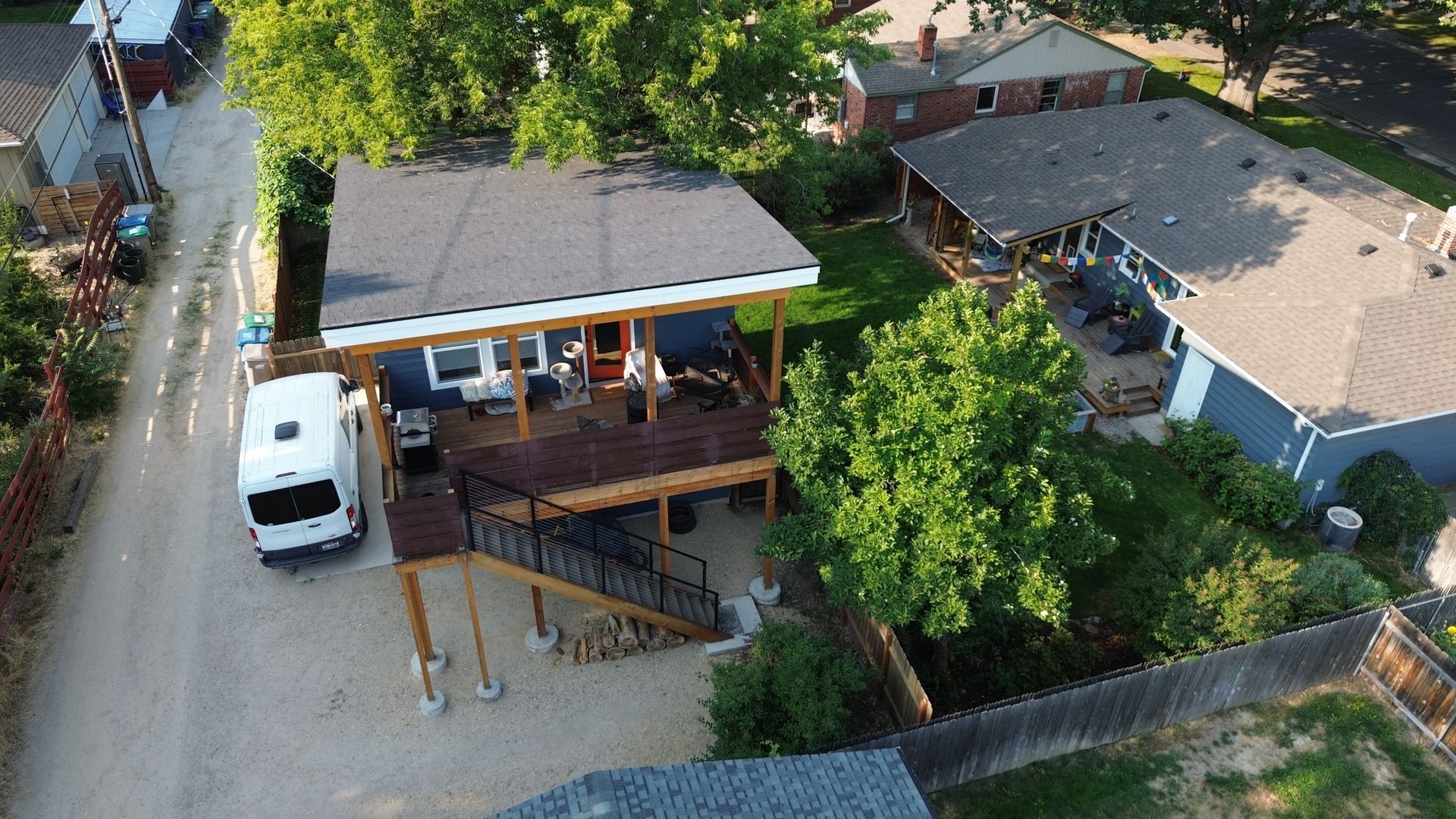 Aerial view of a house with a front porch, white van, and trees in a residential yard.