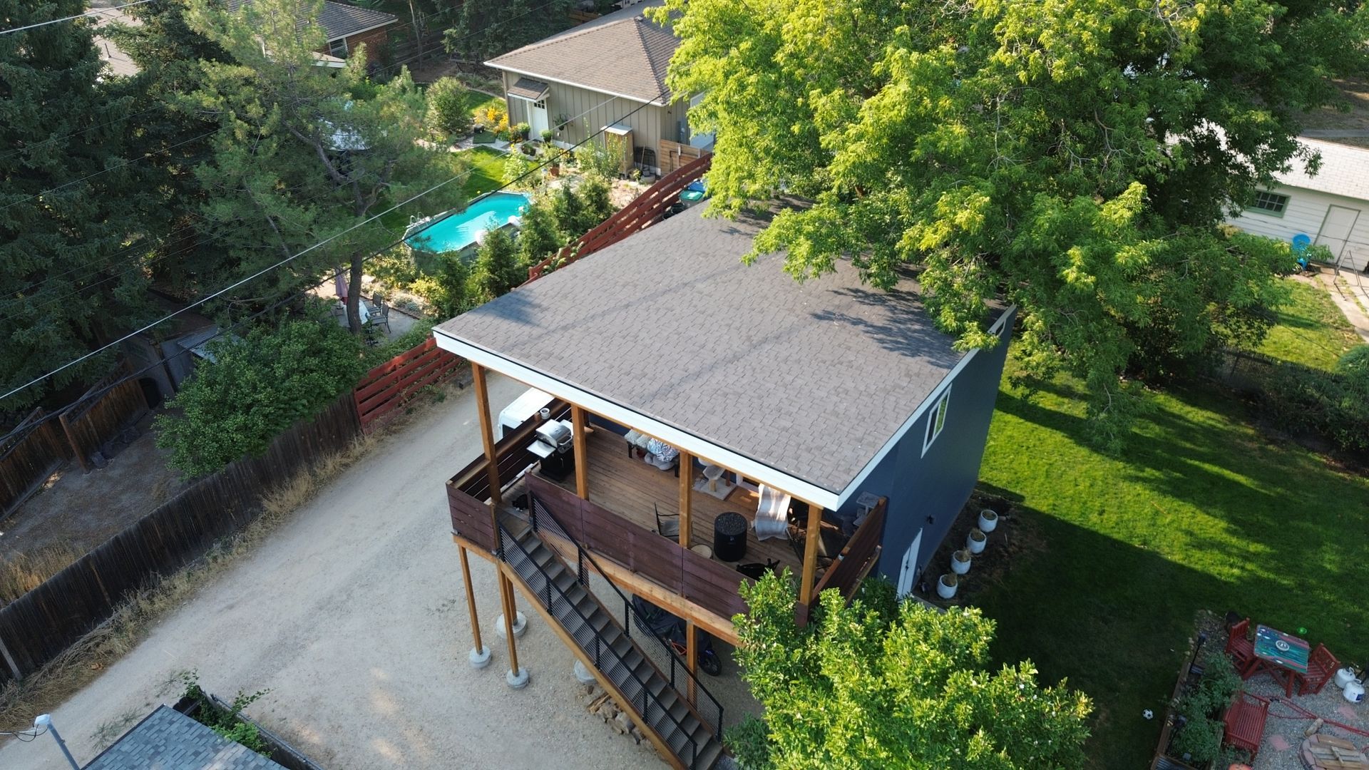 Aerial view of a small house with a porch, surrounded by trees and a yard.