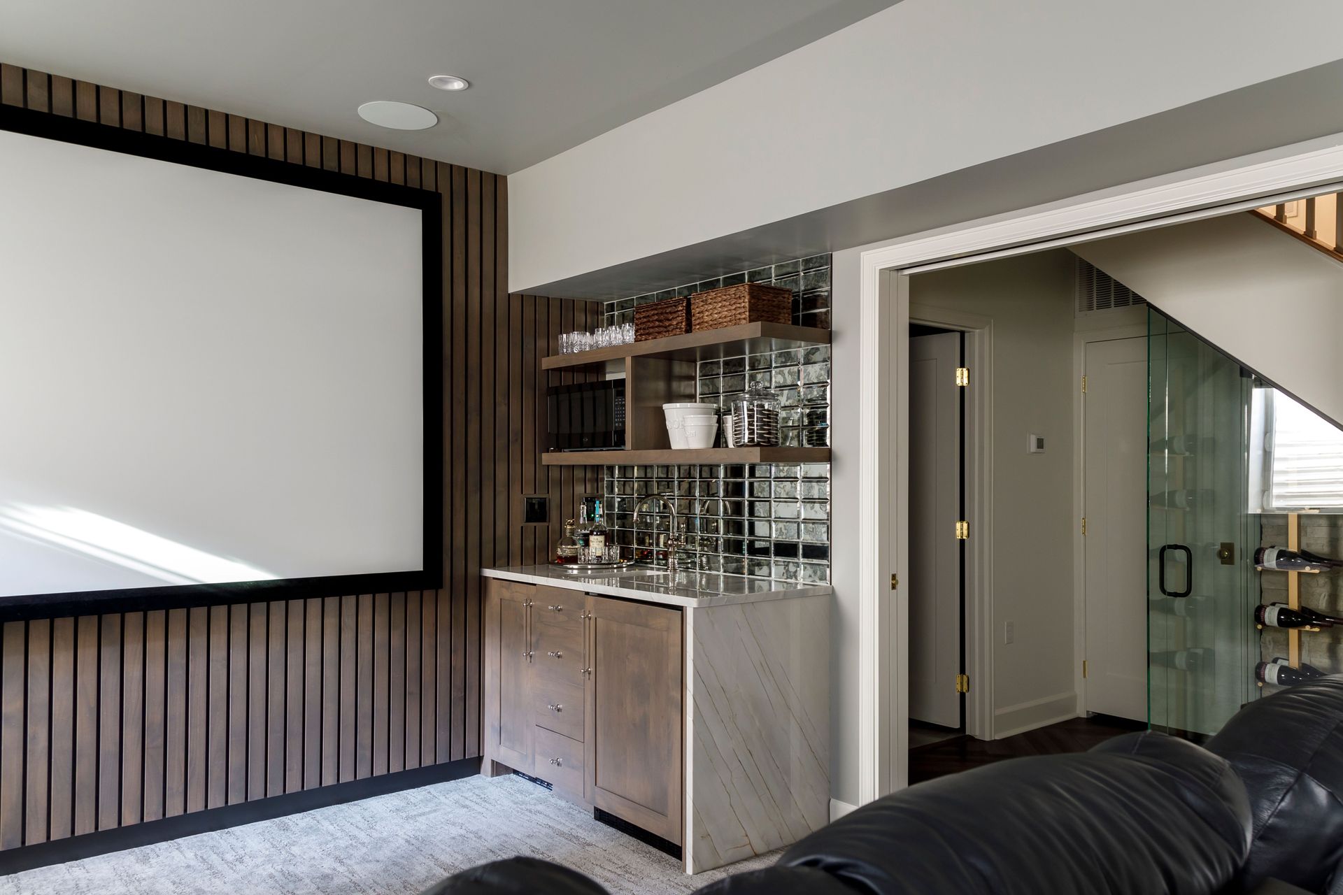 Living room with large projector screen, wood panel wall, bar cabinet, and staircase view
