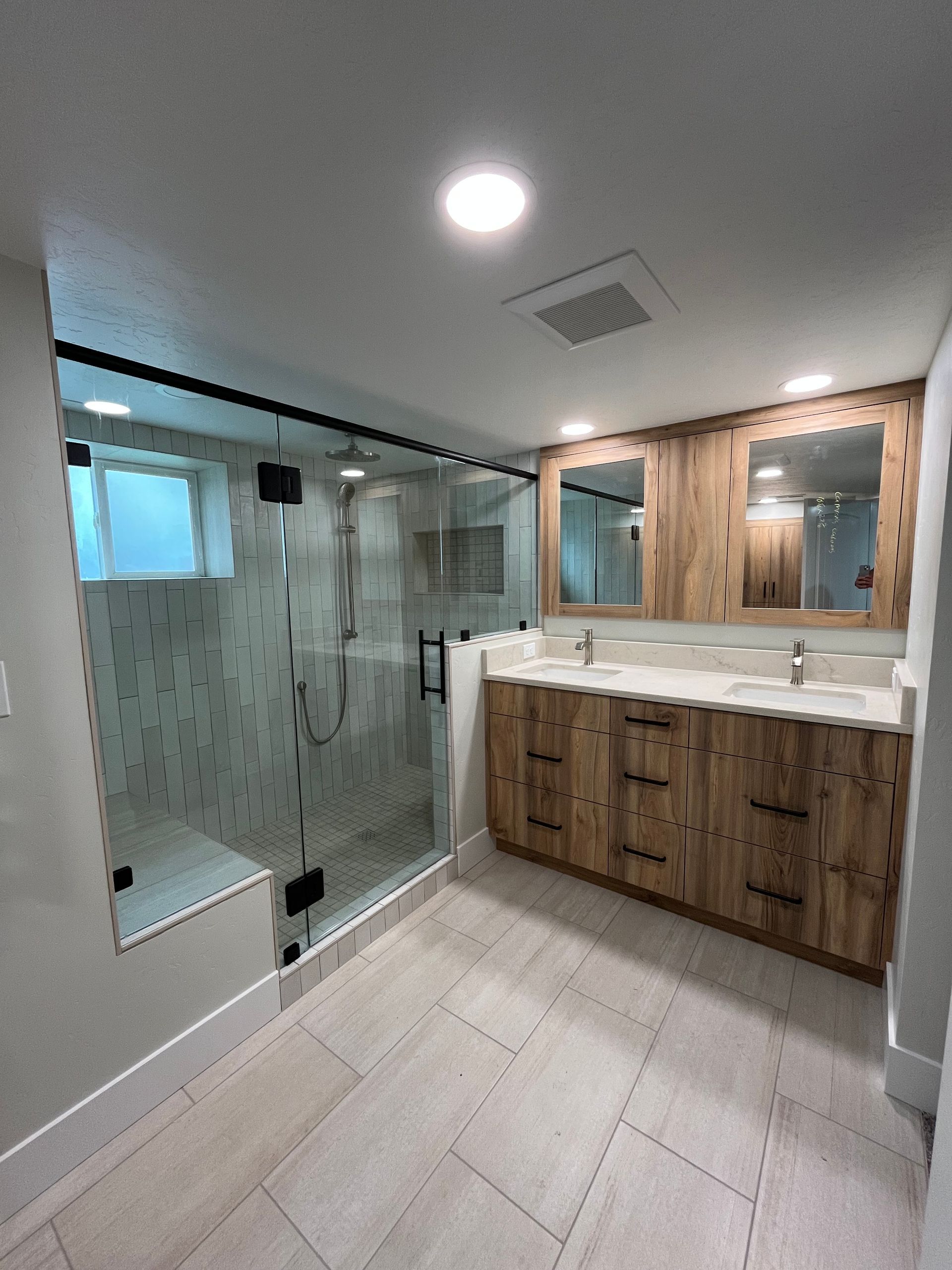 Modern bathroom with glass shower, wood vanity, and large mirror under bright ceiling light