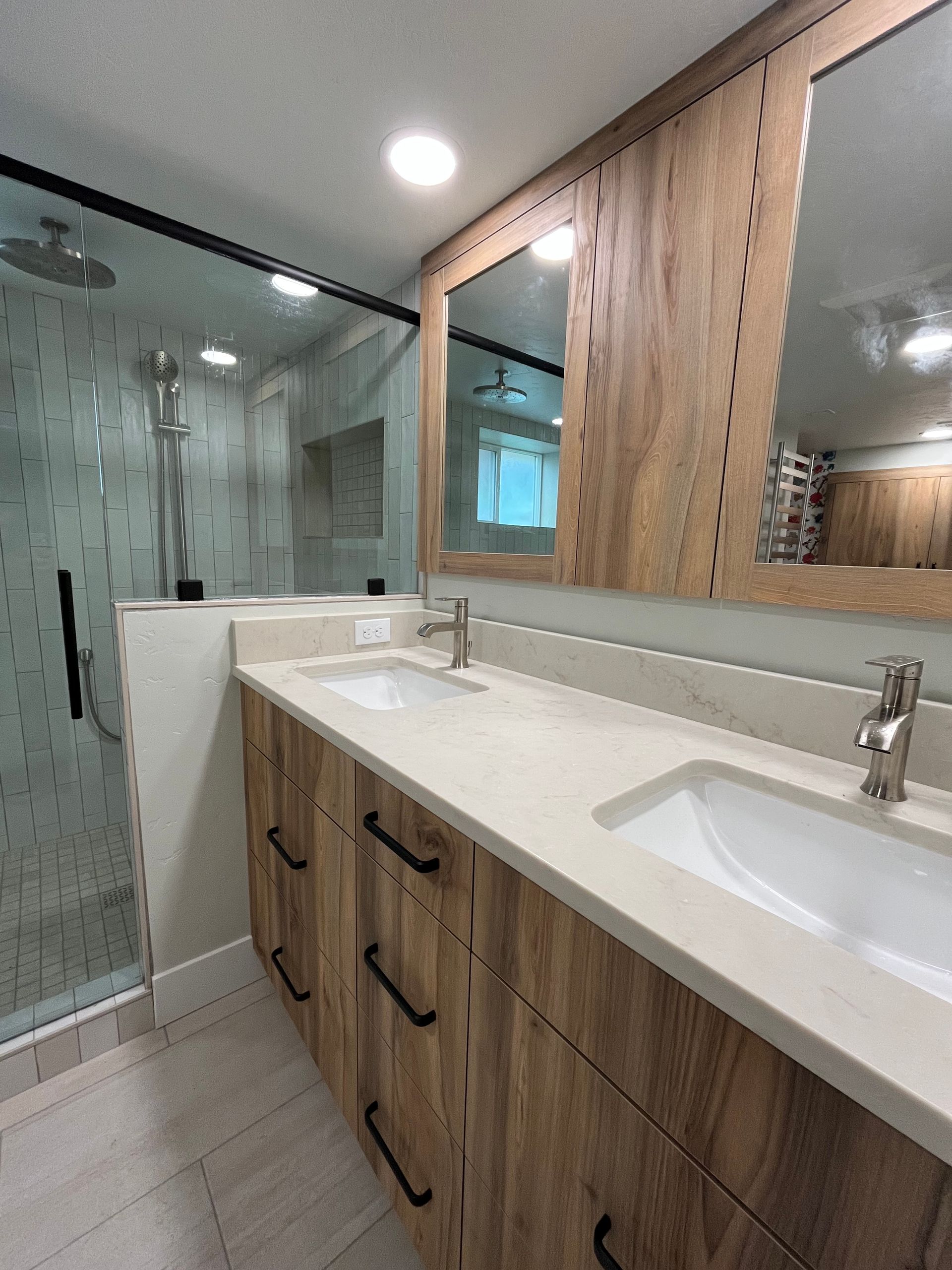 Modern bathroom with wood vanity, white sink, large mirror, and glass-enclosed shower