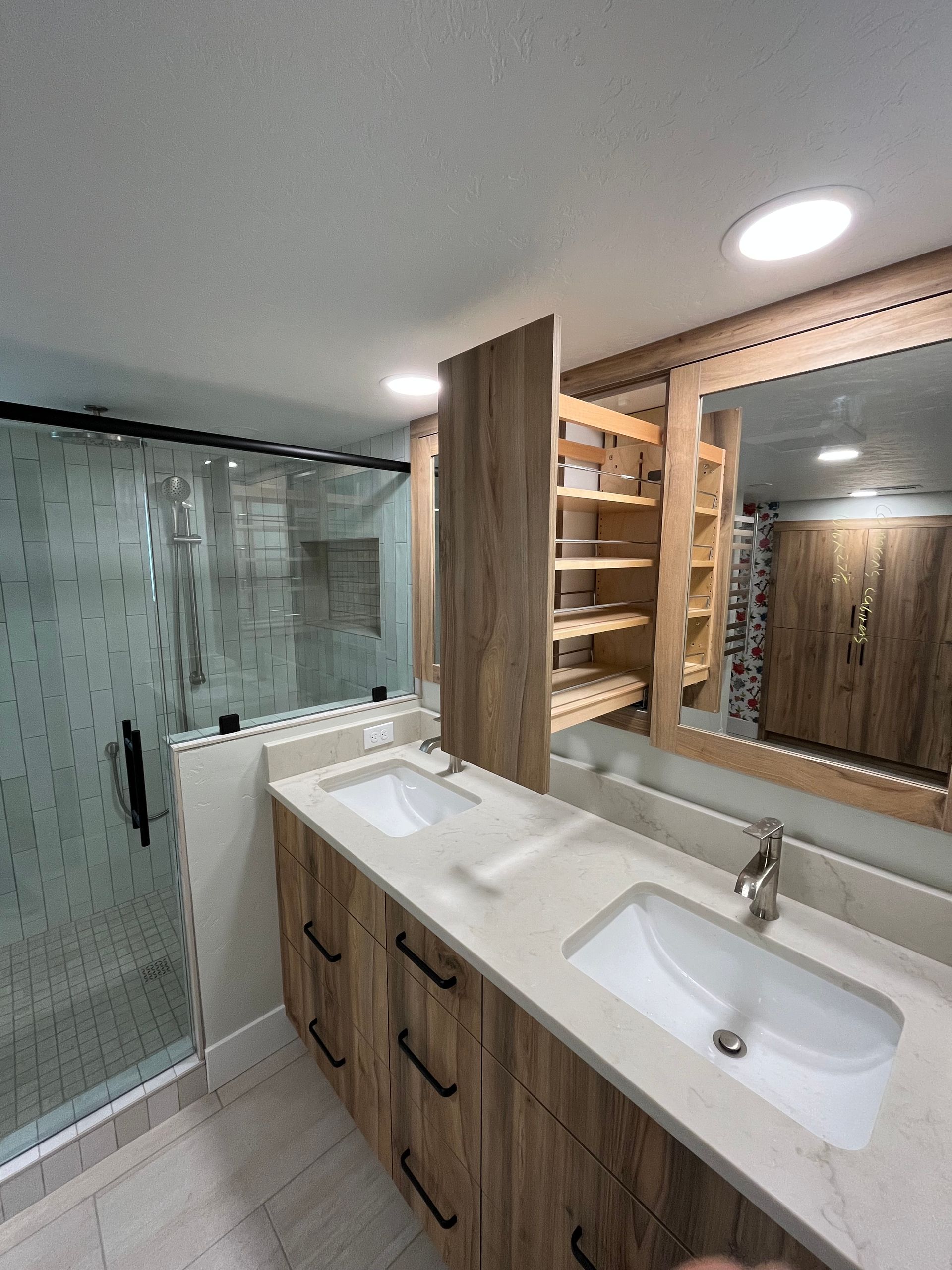 Modern bathroom with double sink vanity, large mirror, wood cabinets, and glass shower enclosure.