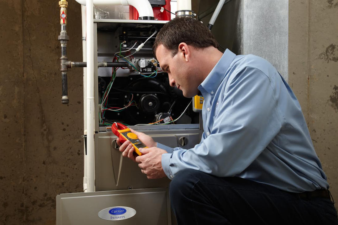 Technician inspecting furnace with multimeter beside a water heater in a utility room