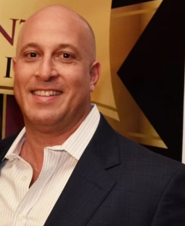 A man in a suit and white shirt is smiling for the camera.