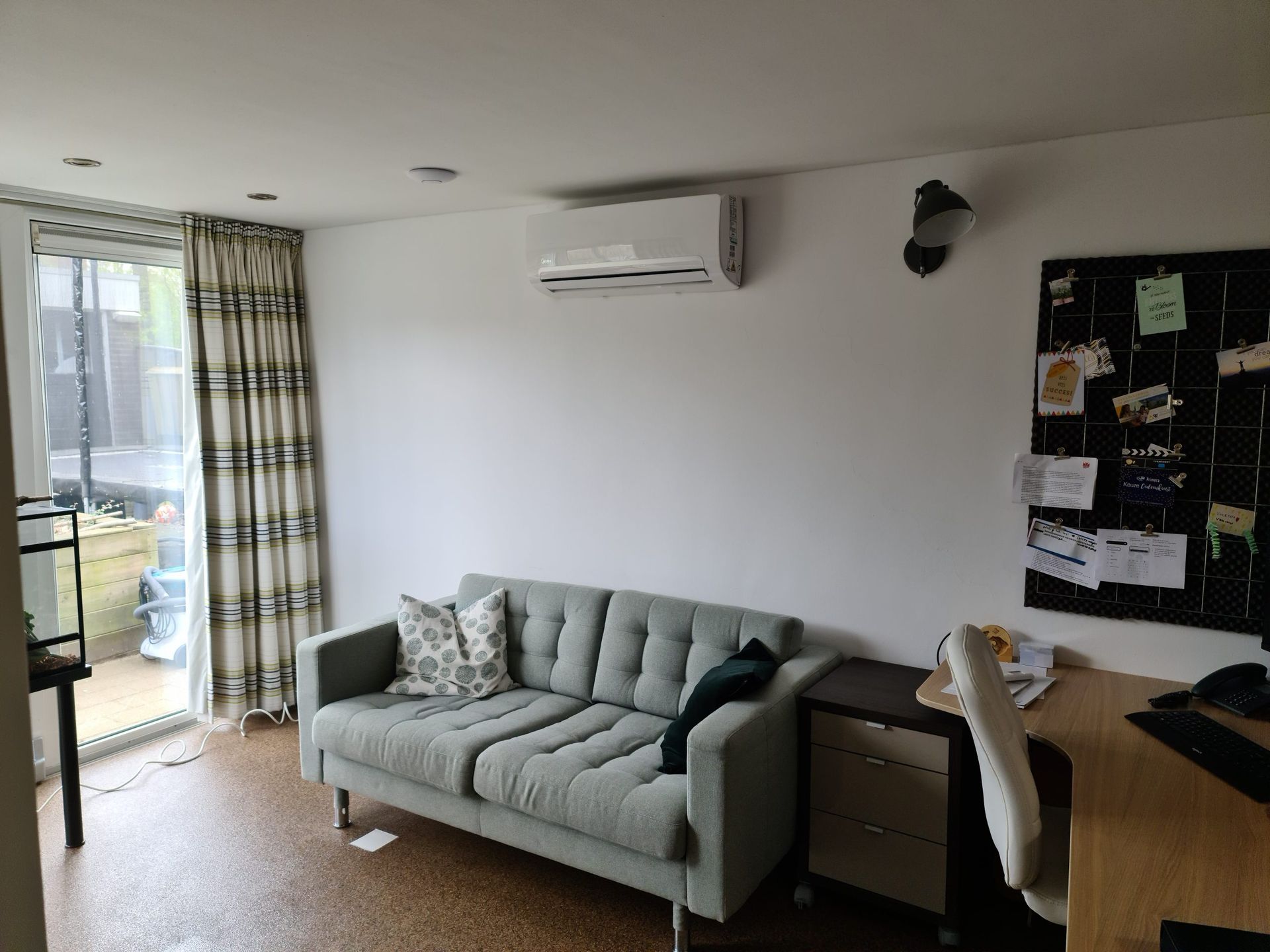 Een woonkamer met een bank, bureau, stoel en airconditioning.