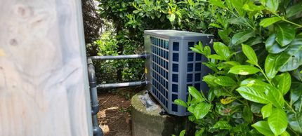Een zwarte airconditioner staat naast een struik.