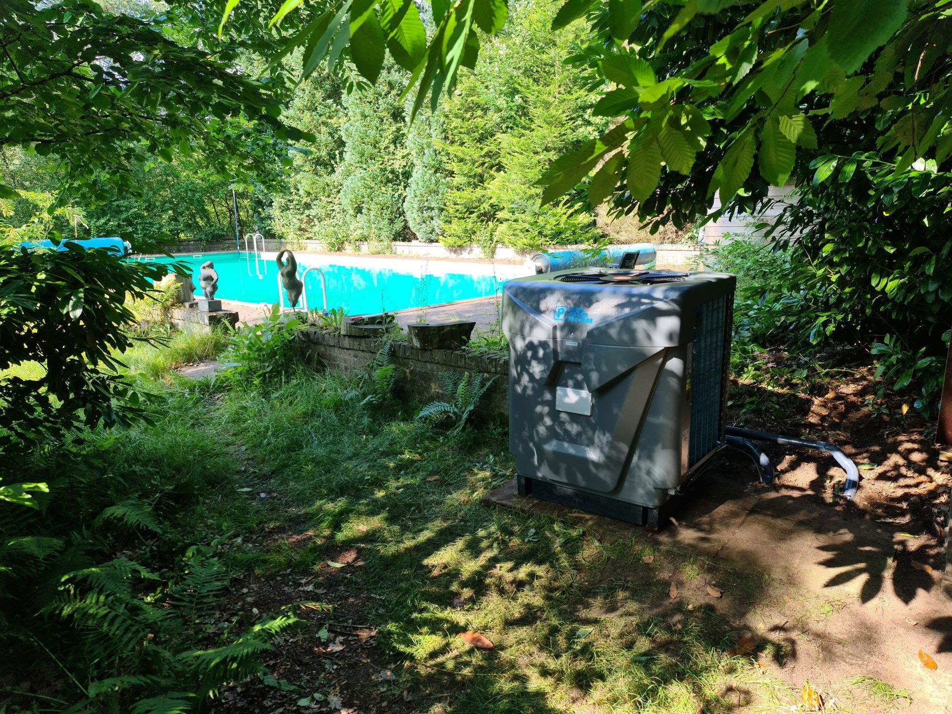 Een airconditioner staat in het gras voor een zwembad.