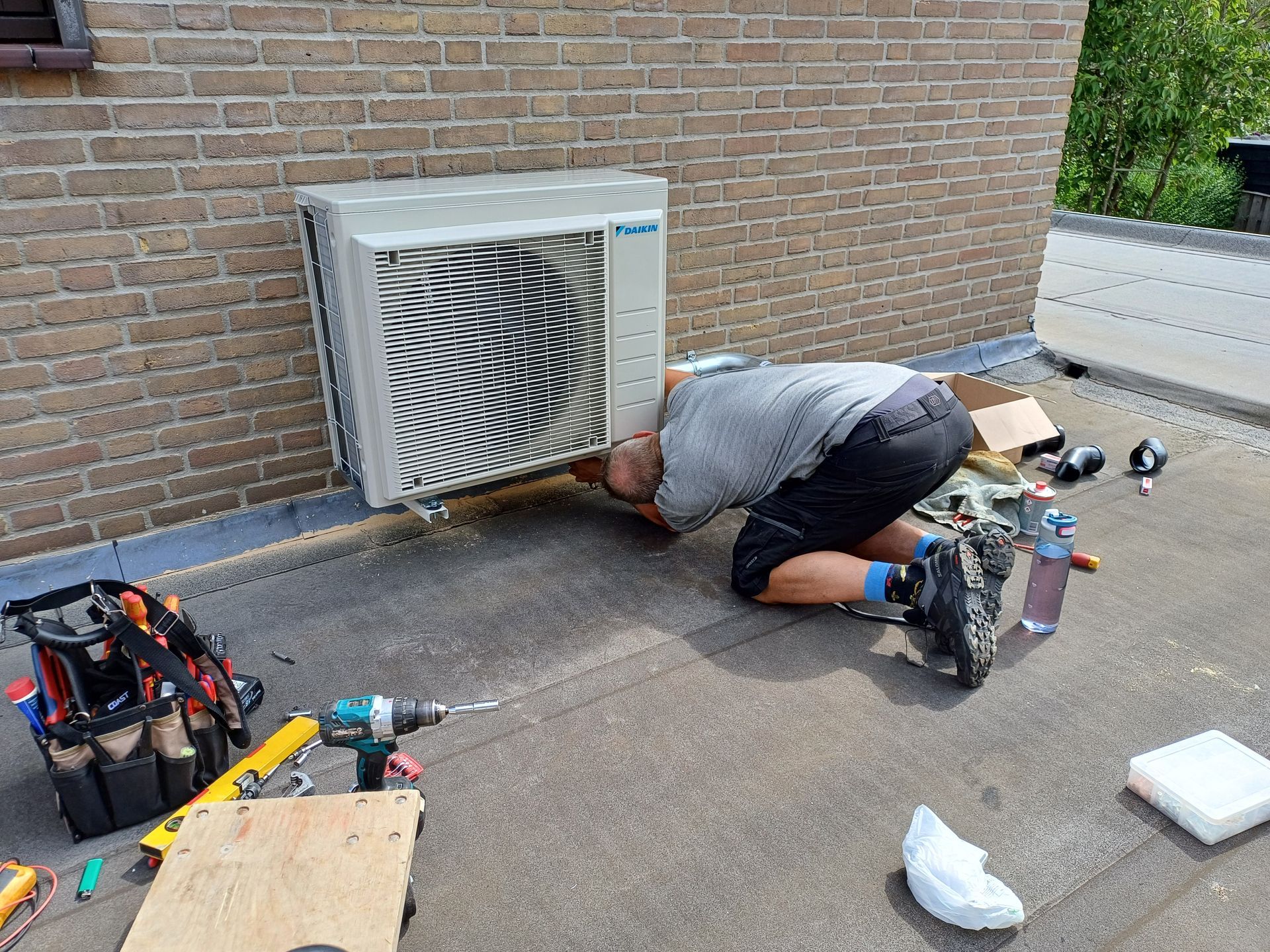 Monteur voert service en onderhoud uit aan een Daikin airconditioning buitenunit op een plat dak, omringd door gereedschap en onderdelen.