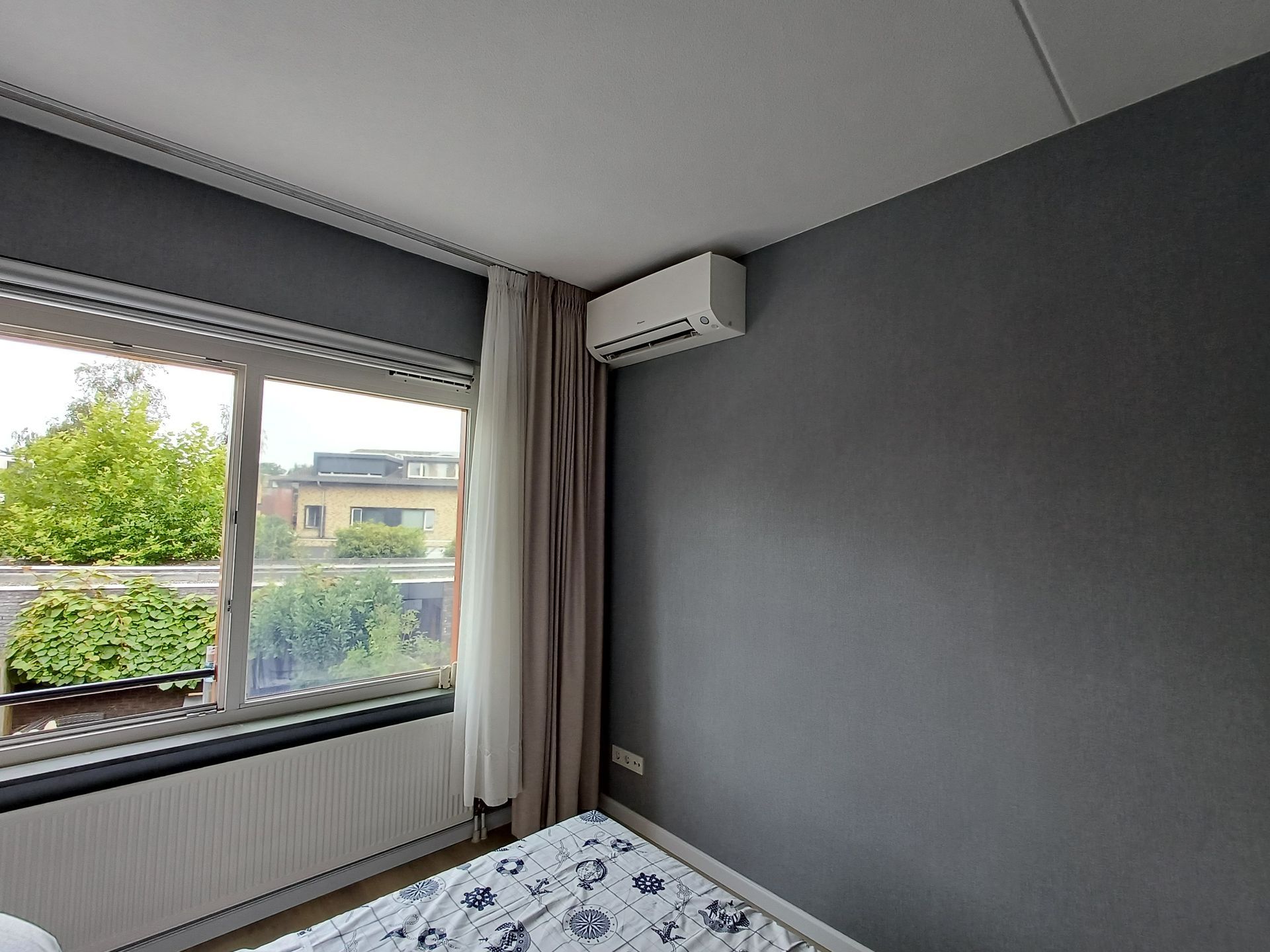 Een witte airconditioner staat op een terras naast een bakstenen muur.