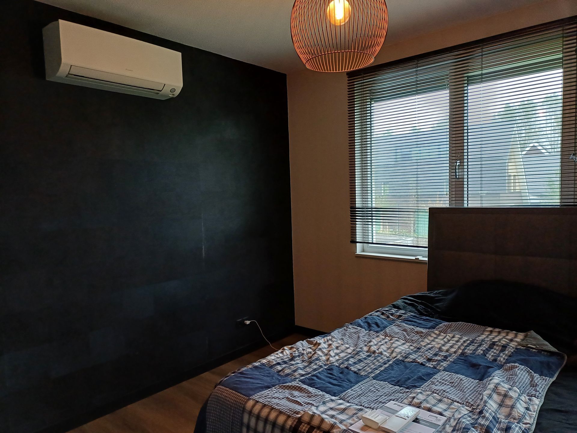 Daikin Perfera wandmodel airco geïnstalleerd in een moderne slaapkamer met donkere accentmuur, houten vloer en raam met jaloezieën.
