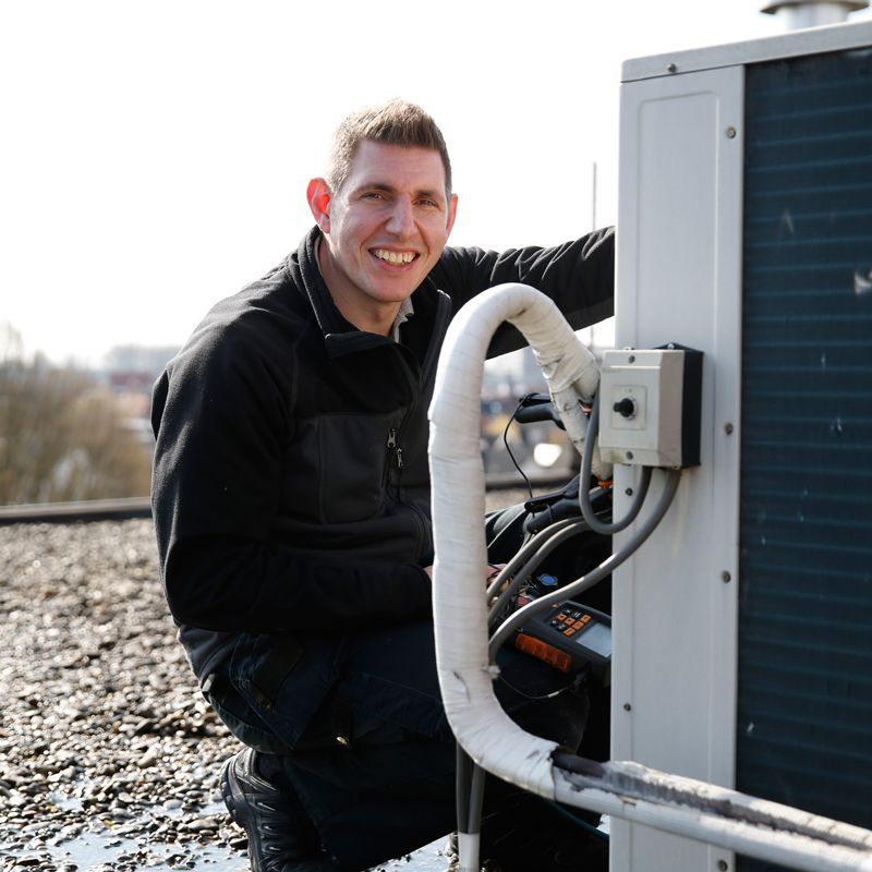 Een man in een zwart jasje werkt aan een airconditioner