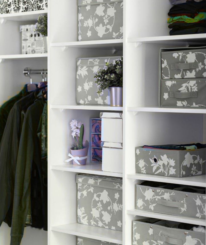 White closet organizer with folded clothes, hanging garments, and patterned storage boxes with flowers and decor.