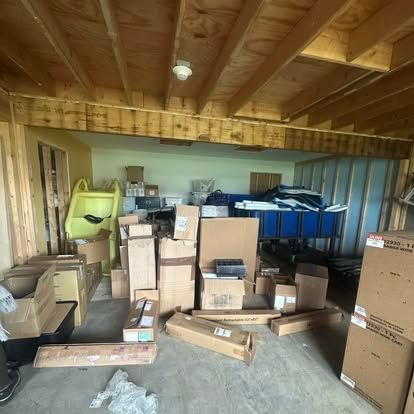 A cluttered garage under construction, filled with numerous cardboard boxes, a yellow plastic slide, and blue storage.