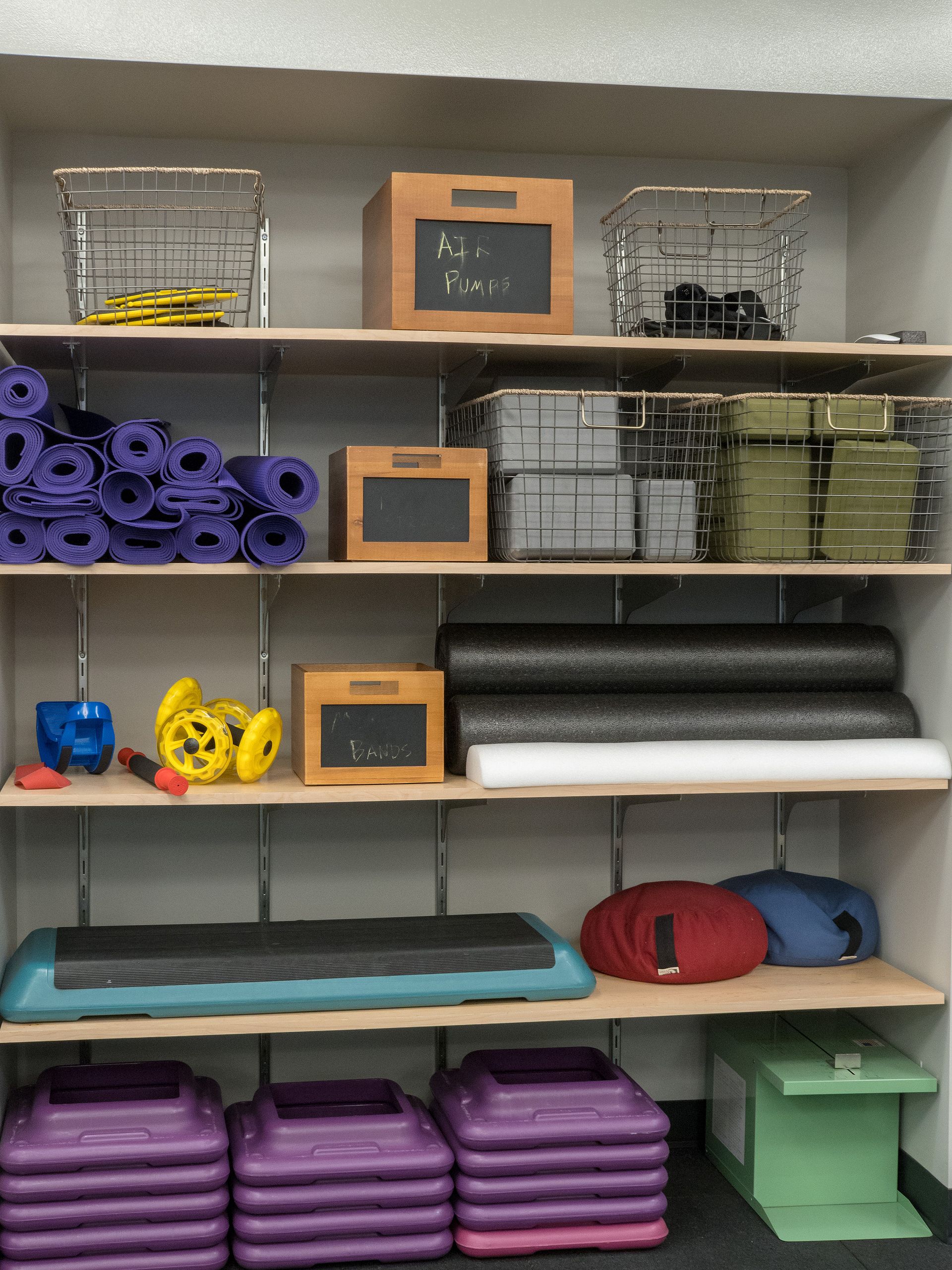 Shelves with fitness equipment: yoga mats, steps, weights, foam rollers, and boxes.