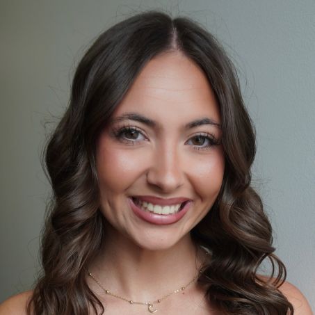 Woman with dark hair smiling, wearing a black off-the-shoulder top, wooden background.