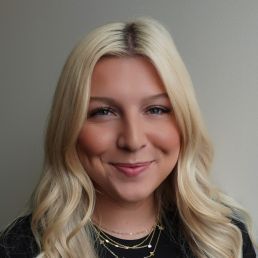 Blonde woman with a slight smile against a wood-paneled background.