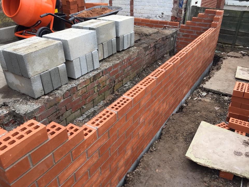 A brick wall is being built next to a cement mixer.