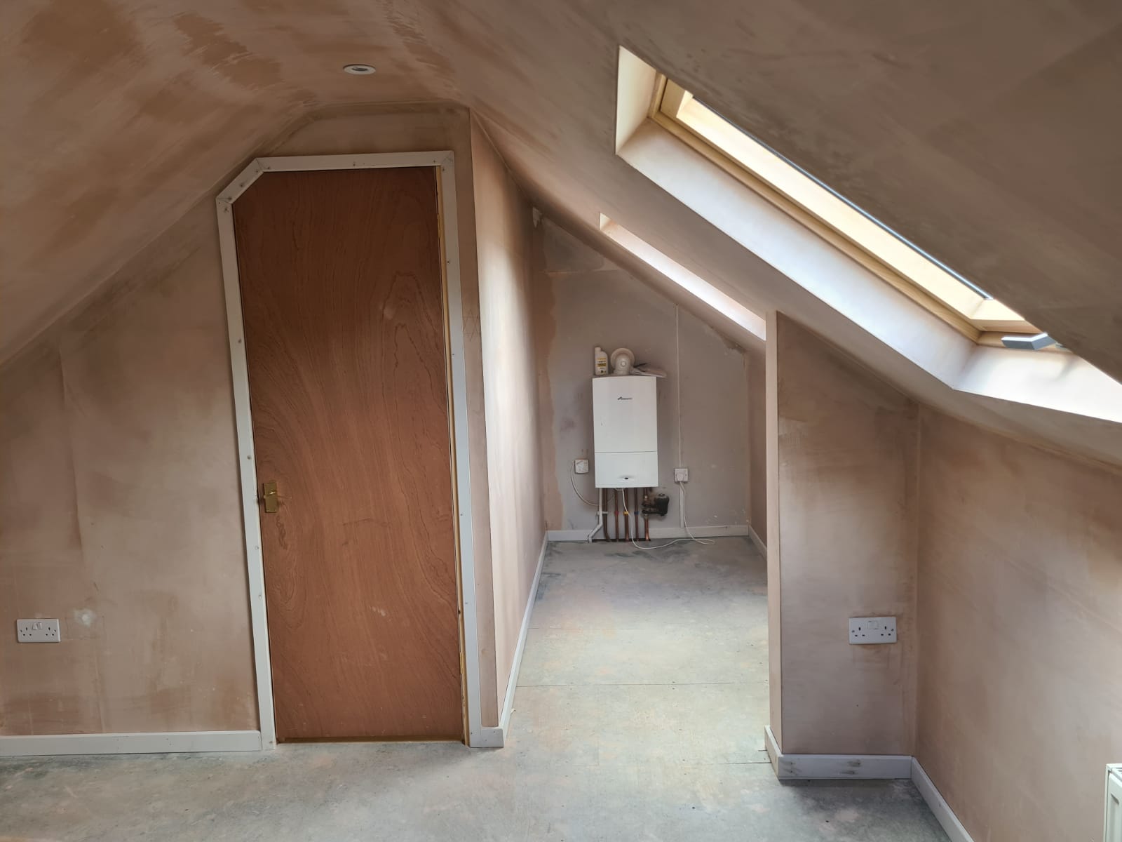 An empty attic with a skylight and a door.