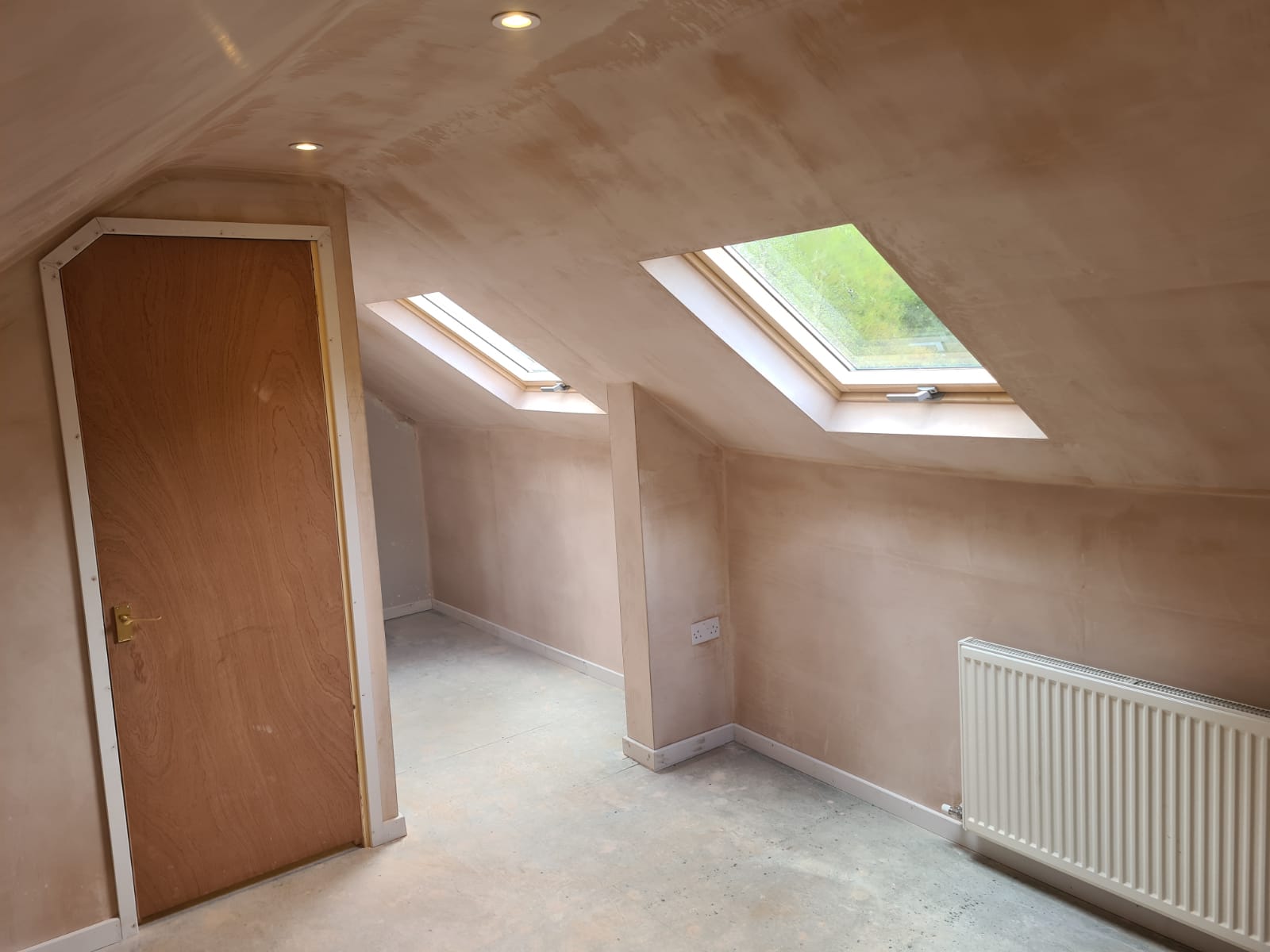 An empty attic with a skylight and a door.
