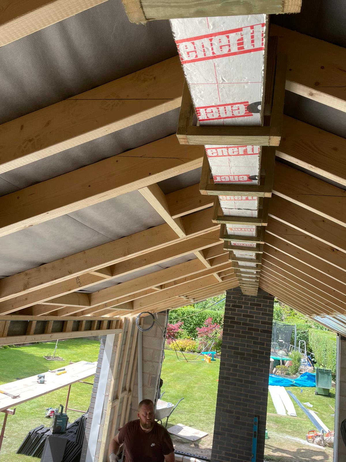 A man is standing under a wooden roof in a building under construction.