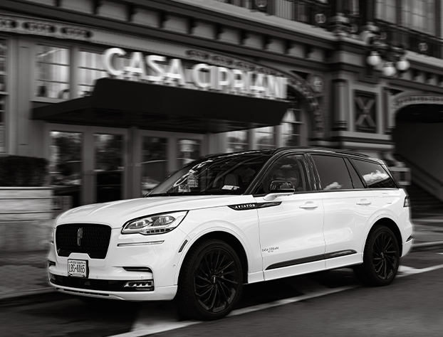 A black and white photo of a white car parked in front of a building.