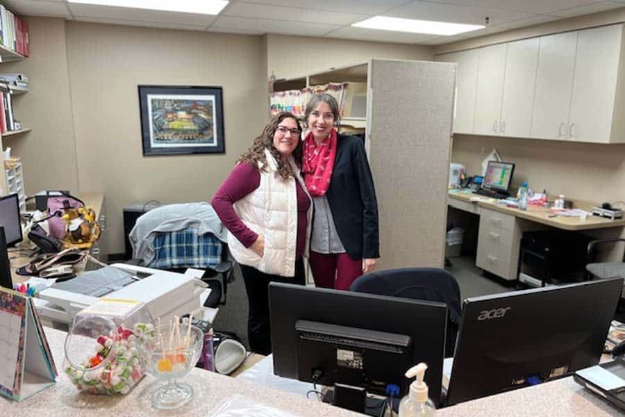 Two women are posing for a picture in an office.