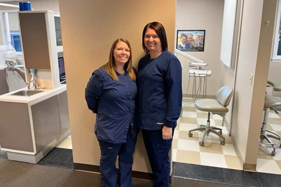 Two female dental assistants are standing next to each other in a dental office.