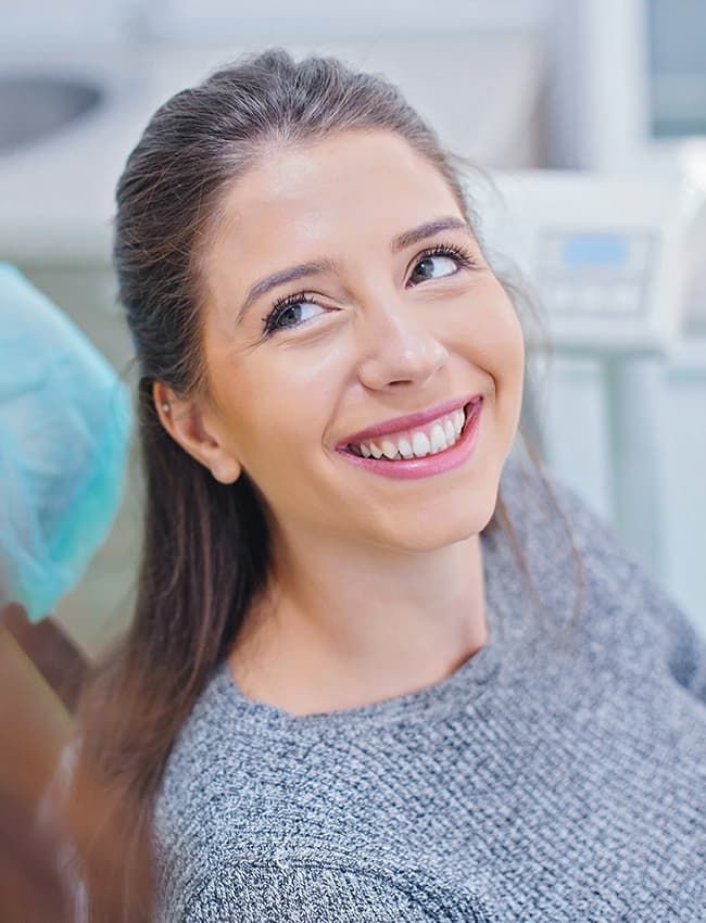A woman is smiling while sitting in a dental chair.