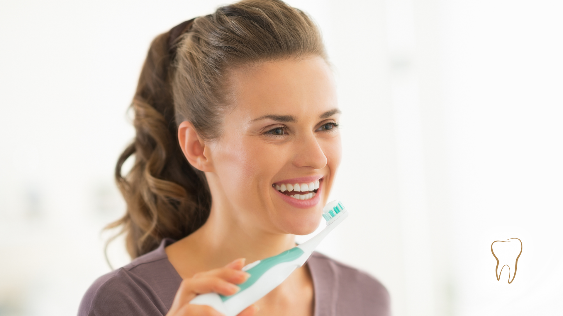 Woman smiling while brushing teeth with an electric toothbrush in a bathroom setting.