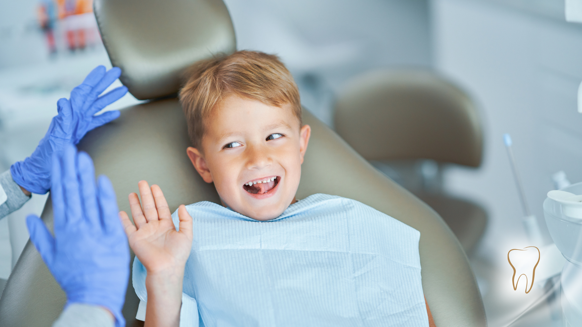 Boy in dentist chair gives high-five with gloved hands; smiling; tooth icon.