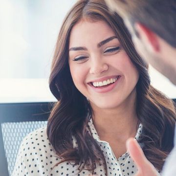 A woman in a polka dot shirt is smiling while talking to a man